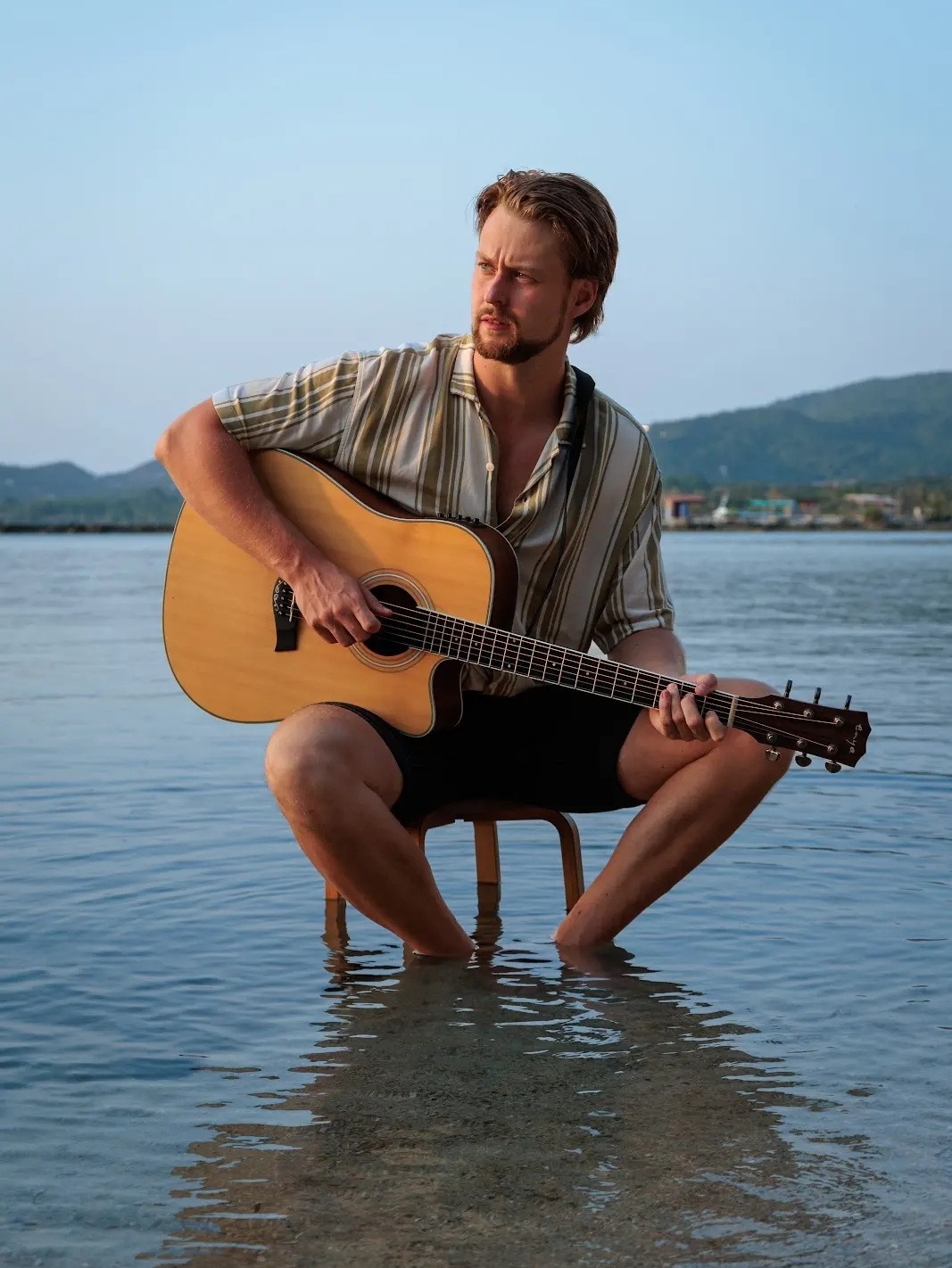 Jesper Wolthers playing guitar, sitting in shallow water by the sea